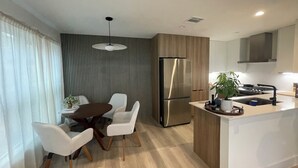 Una cocina moderna con una isla central, electrodomésticos de acero inoxidable y un comedor con sillas blancas.
