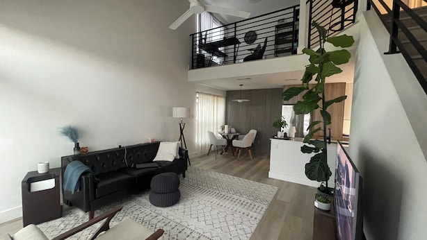 Un amplio salón con un sofá negro, una mesa de comedor y una escalera que sube a un nivel superior.