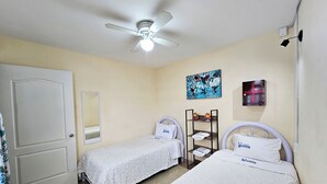 A hotel room with two single beds, a ceiling fan, a painting, a shelf with toiletries, and a door. - Apartment in Tehuacan 2 bedrooms, WiFi, equipped kitchen and close to downtown (Tehuacán)