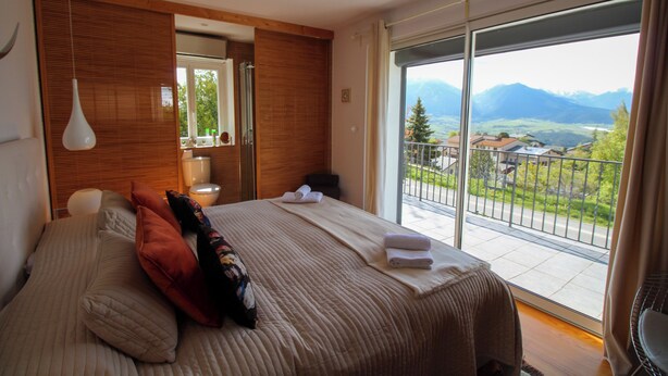 A bedroom with a large bed, a wooden headboard, a hanging light fixture, and a view of mountains through a sliding glass door. - La Villa de Font-Romeu (Font-Romeu-Odeillo-Via)