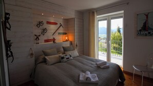 A bedroom with a large bed, a view of the outdoors through a sliding glass door, and a wooden wall with various decorations. - La Villa de Font-Romeu (Font-Romeu-Odeillo-Via)