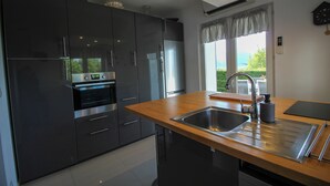 A modern kitchen with dark cabinets, stainless steel appliances, a wooden countertop, and a window with a view. - La Villa de Font-Romeu (Font-Romeu-Odeillo-Via)