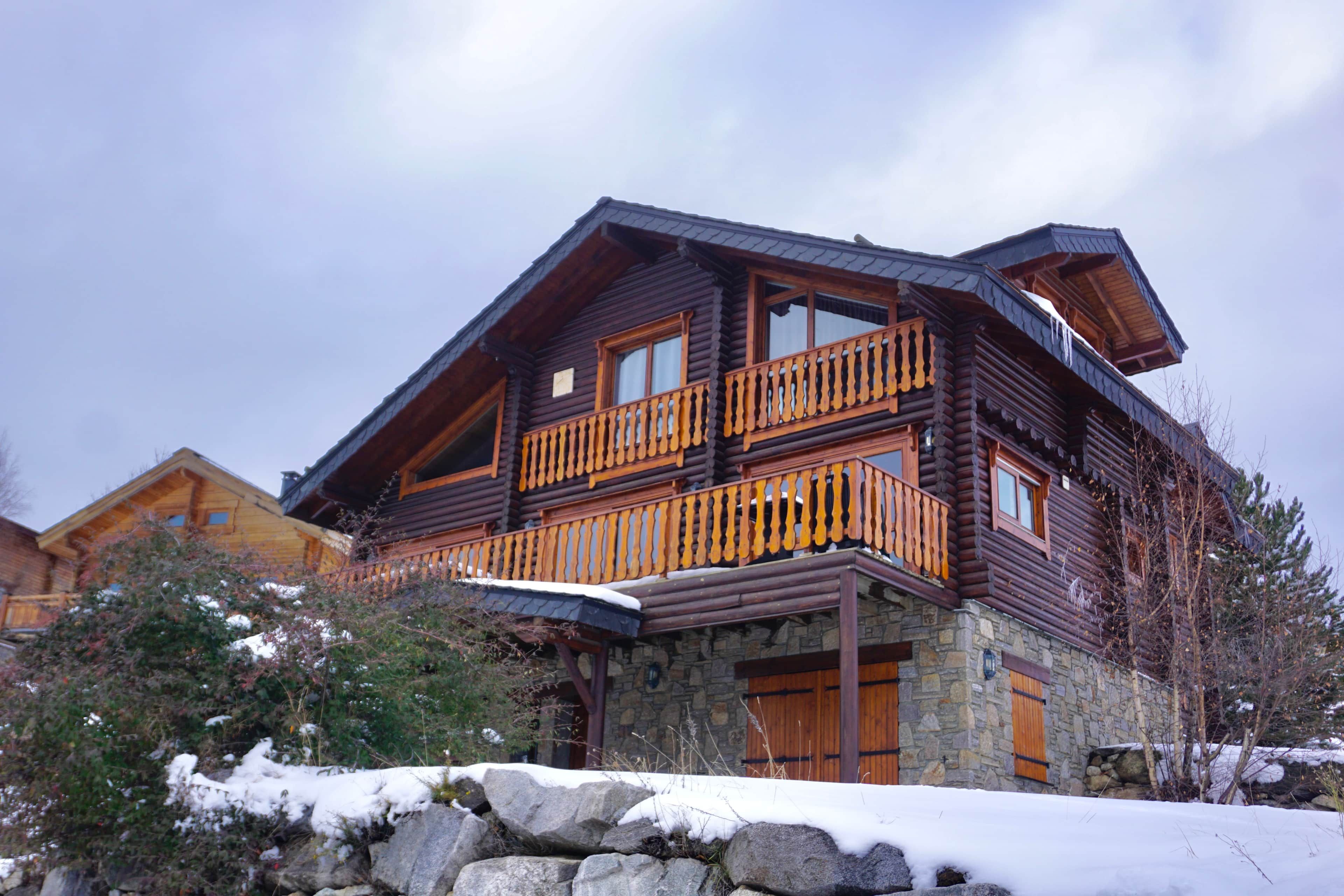 A log cabin with a stone foundation, wooden balcony, and a stone wall in front.