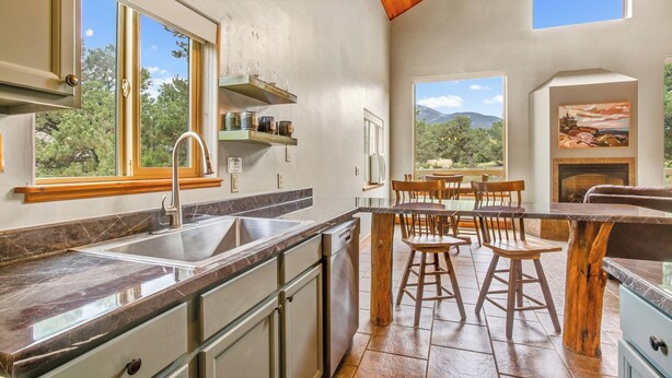 A kitchen with a large window, a sink, and a dining area with stools. - Salida CO Rentals - Home nestled in the trees, 5 minutes from downtown Salida (Salida)
