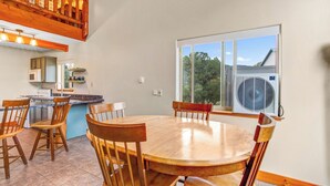 A dining area with a round wooden table and chairs, a kitchen with a microwave and cabinets, and a large window with a view of trees and a house. - Salida CO Rentals - Home nestled in the trees, 5 minutes from downtown Salida (Salida)