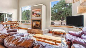 A spacious living room with leather sofas, a fireplace, large windows, and a television. - Salida CO Rentals - Home nestled in the trees, 5 minutes from downtown Salida (Salida)