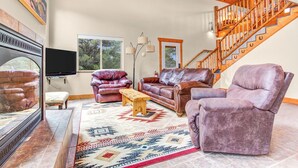 A spacious living room with a large TV, leather sofas, a wooden coffee table, and a patterned rug. A wooden staircase is visible in the background. - Salida CO Rentals - Home nestled in the trees, 5 minutes from downtown Salida (Salida)