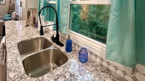 A kitchen with granite countertops, a stainless steel sink, and a window with teal curtains. - Chic 2BR/2BA Near Dining & Shops (Winston-Salem)