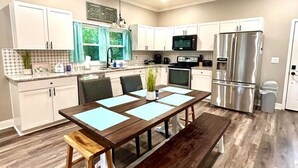 A modern kitchen with white cabinets, a stainless steel refrigerator, and a wooden dining table with benches. - Chic 2BR/2BA Near Dining & Shops (Winston-Salem)
