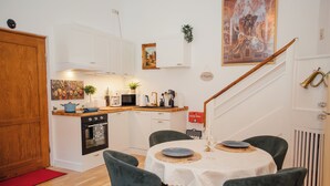 Cocina compacta con armarios blancos, puerta de madera y comedor con mesa redonda y sillas verdes.