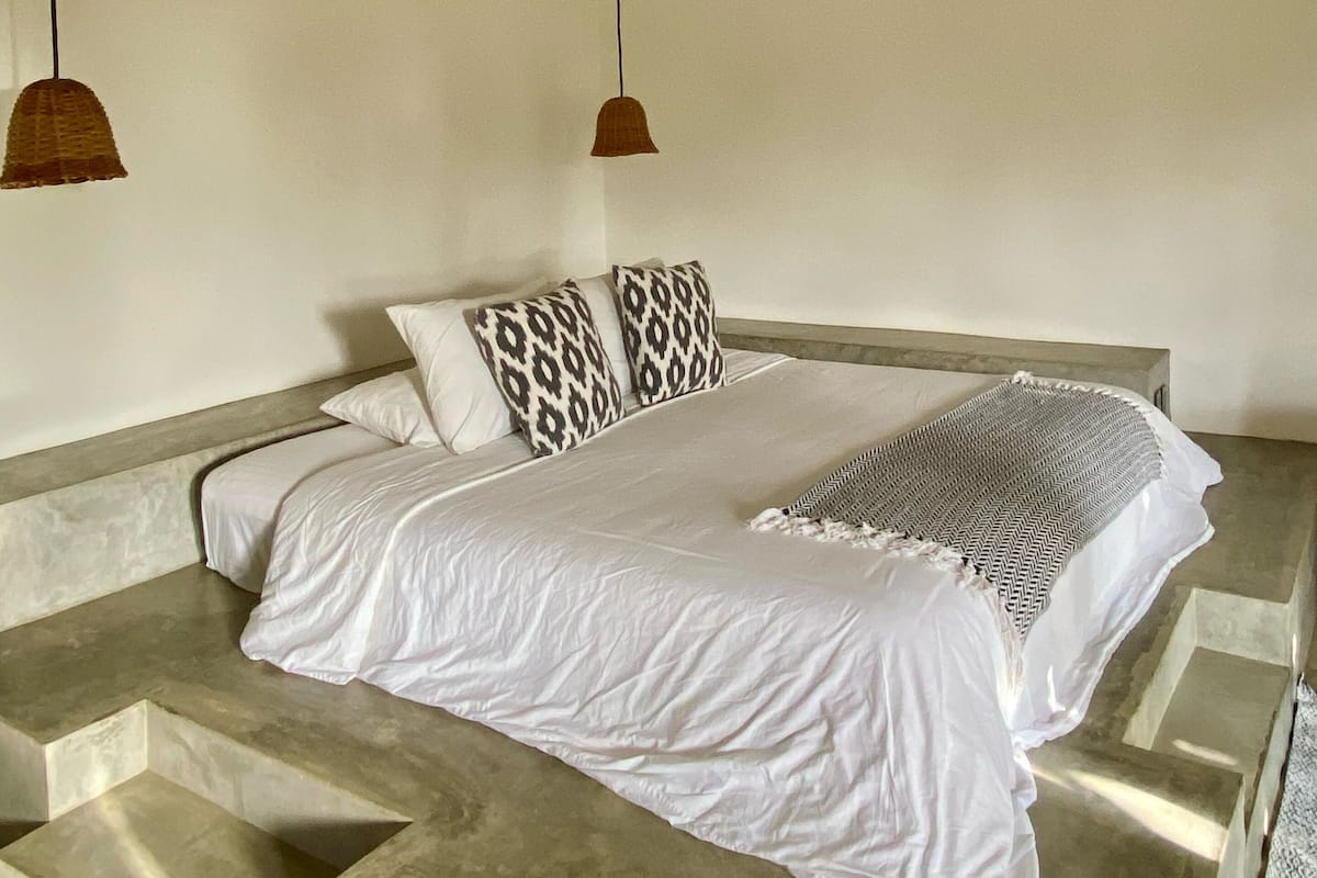 A bedroom with a bed, patterned pillows, a ceiling fan, and a window.