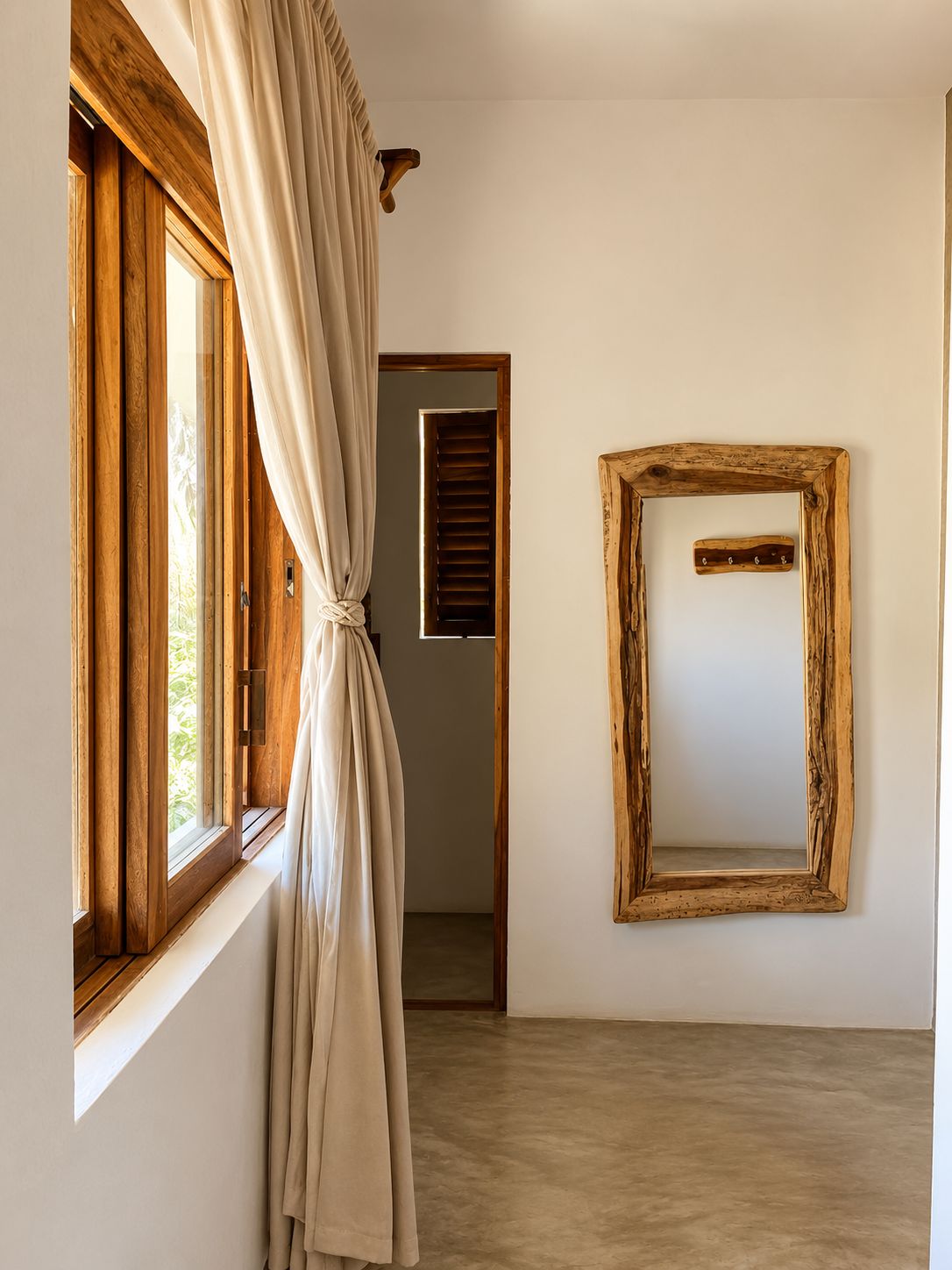 A room with a large window, a wooden door, and a mirror on the wall.