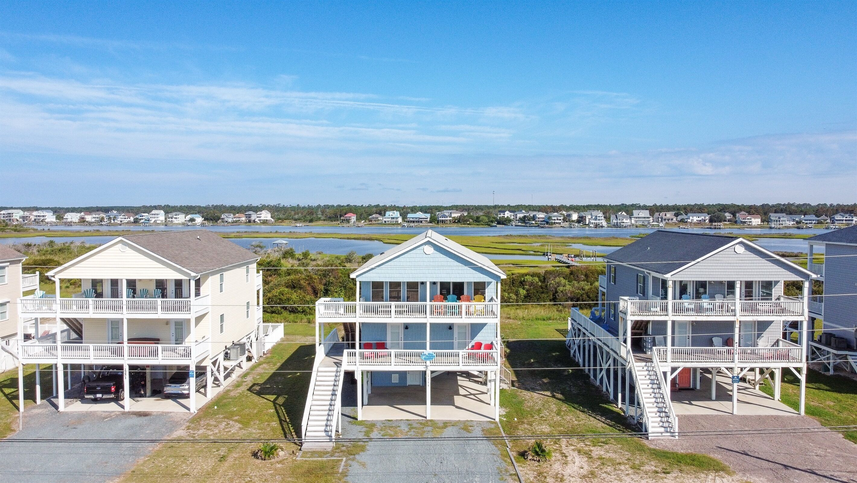 A row of beach houses with balconies, a dock, and a view of the water and distant houses.