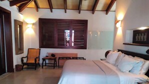 A bedroom with a bed, a desk, and a chair. There are wall-mounted lights and a window with shutters.