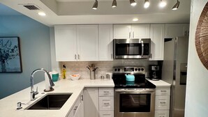 Une cuisine moderne avec des meubles blancs, des appareils en acier inoxydable, un évier double et un sol carrelé disposé en motif chevron.