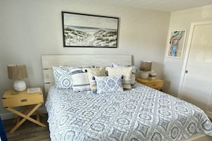 A bedroom with a bed, a nightstand, a lamp, and a framed picture on the wall.