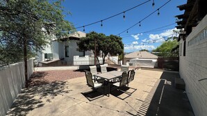 A patio with a table and chairs, a barbecue grill, and a string of lights.