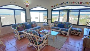 A room with wicker furniture, a glass coffee table, and large windows offering a view of the ocean. - 10 Minute Walk to Pickleball and the Sea of Cortez (Los Barriles)