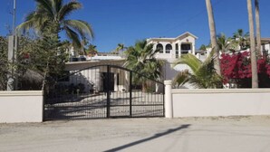 A gated residential area with a large house, palm trees, and a clear sky. - Cozy Home One Off the Beach (Spa Buena Vista)