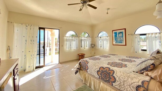 A spacious bedroom with a large bed, a ceiling fan, and a view of the outdoors through a sliding glass door. - Cozy Home One Off the Beach (Spa Buena Vista)