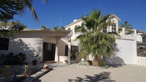 A two-story house with a white exterior, a covered patio, and a palm tree in the front yard. - Cozy Home One Off the Beach (Spa Buena Vista)