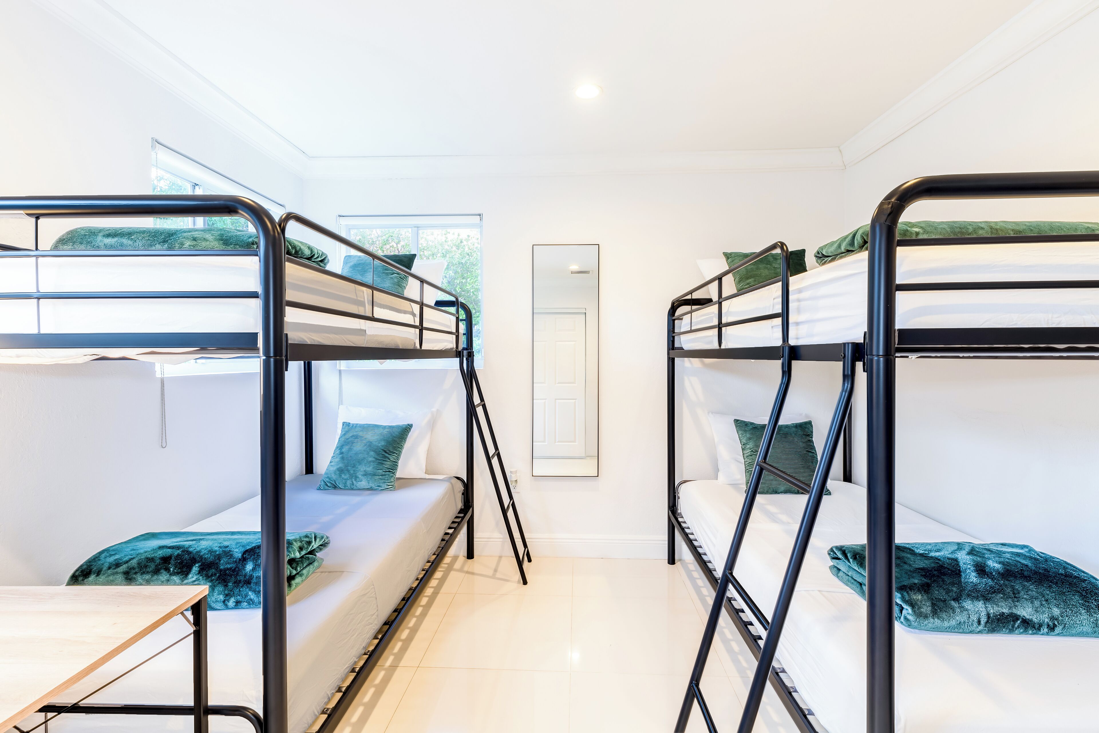 A dormitory room with bunk beds, a small table, and a window providing natural light.