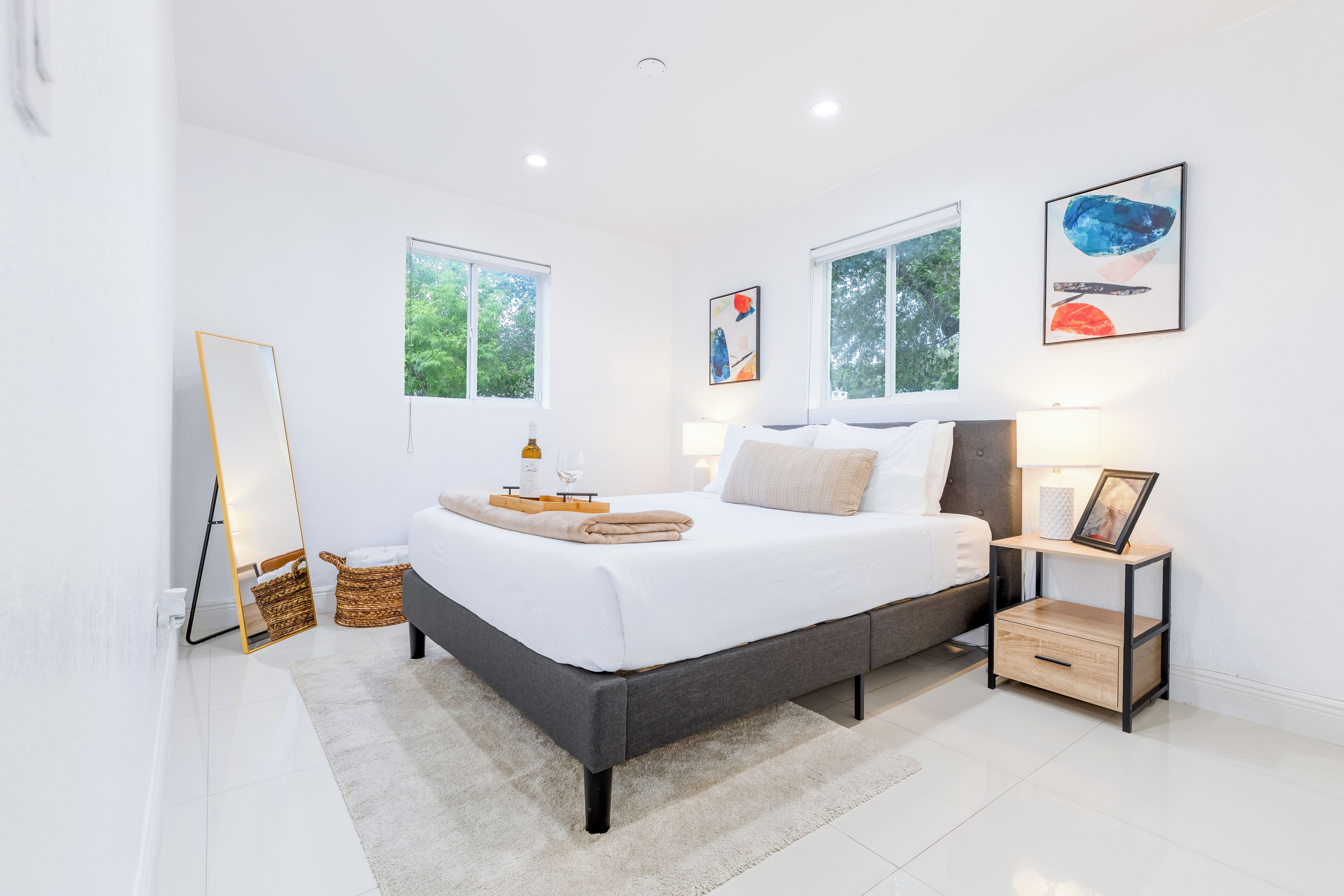 Ein modernes Schlafzimmer mit einem großen Bett, Nachttischen, einem Spiegel und Kunstwerken an den Wänden.