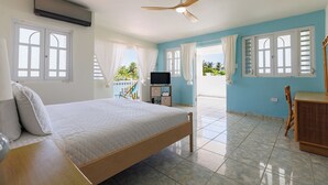 A bedroom with a bed, a ceiling fan, a TV, and a view of the outdoors.