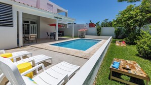 A backyard with a swimming pool, lounge chairs, a dining area, and a small garden.