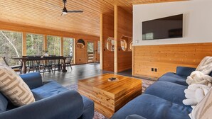 Amplia sala de estar con techo de madera, una mesa de comedor con sillas, un sofá grande y un televisor montado.