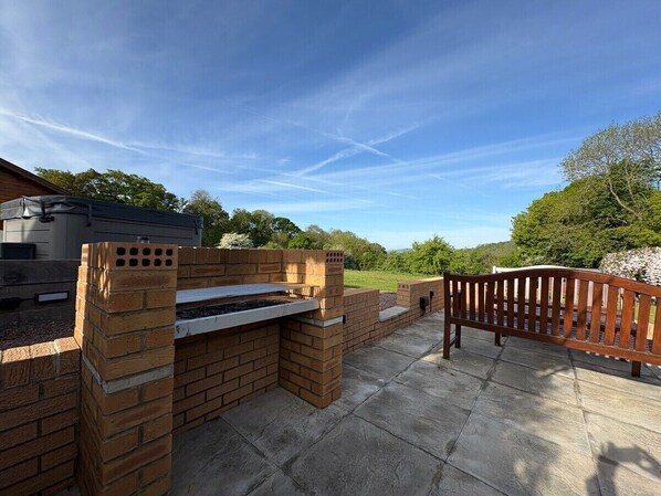 Eine Terrasse im Freien mit Grill, Ziegelmauern und einer Holzbank.