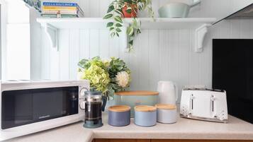 Une cuisine équipée d’un four à micro-ondes, d’une machine à café, de pots à sucre et à café, d’un grille-pain et d’une plante en pot.