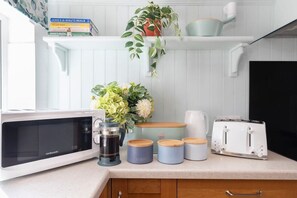 Una cocina equipada con microondas, cafetera, recipientes para azúcar y café, tostadora y una planta en maceta.