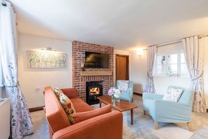 A cozy living room with a brick fireplace, two sofas, a coffee table, and a television mounted above the fireplace. - Beautiful Danford House & Lodge with Hot Tub (Hartpury)