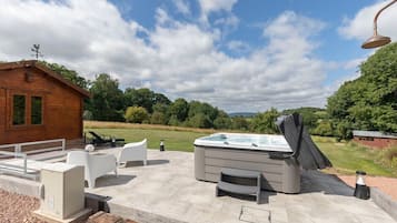 Un bain à remous avec un couvercle, un espace salon extérieur et un chalet en bois situé dans un jardin aménagé.