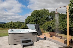 A hot tub with a showerhead, a bench, and a step stool in a garden setting.