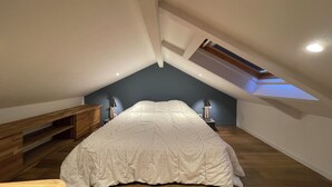 Un dormitorio con techo inclinado, una cama con edredón blanco, dos lámparas de noche y un banco de madera.