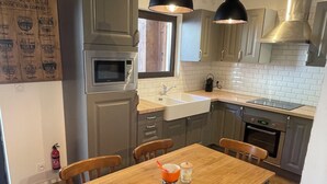 Una cocina moderna con una mesa de comedor de madera, dos lámparas colgantes y electrodomésticos de acero inoxidable.