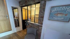 Una habitación con puerta de madera, una silla, una lámpara, un ventanal con vistas y un cartel que dice 'Welcome to our Lake House'.