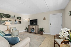 A living room with a sofa, TV, and decorative items. - 1 Min Walk to Beach | Beach Block Oasis | 2BR/1BA (Cocoa Beach)