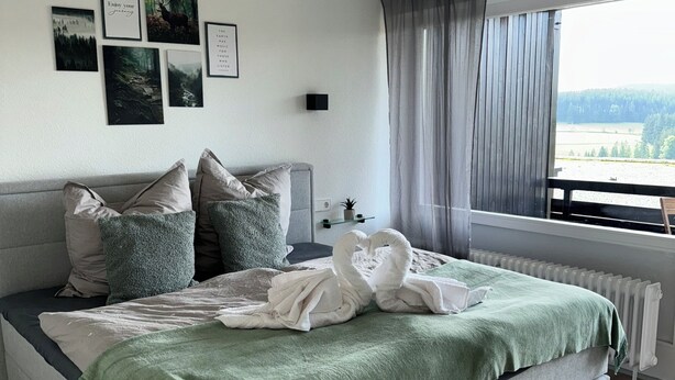 A bedroom with a bed, a window with curtains, and wall art.