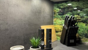 A modern kitchen with a grey textured wall, a wooden cutting board with a candle and a small potted plant, and a knife block with knives.