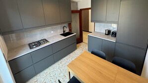 A compact kitchen with grey cabinets, a gas stove, a sink, and a wooden table. - Casa Albenga  (Albenga)