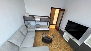 A modern living room with a grey sectional sofa, a small round coffee table, a TV on a stand, and a patterned floor. - Casa Albenga  (Albenga)