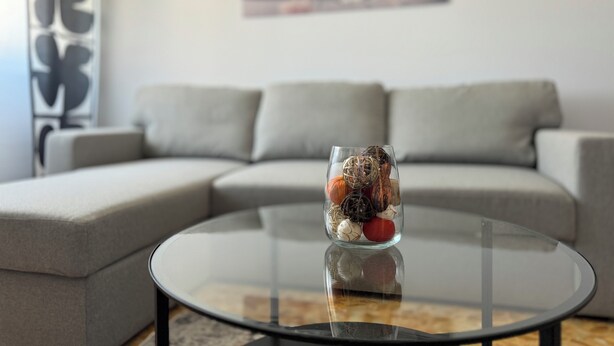 A modern living room with a glass coffee table, a grey sectional sofa, and a decorative vase with stones and a plant. - Casa Albenga  (Albenga)