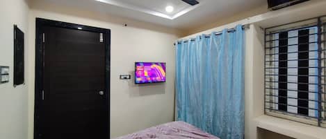 A bedroom with a bed, a ceiling fan, a television, and a window with bars.