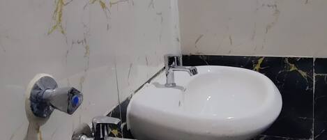 Een badkamer met een witte wastafel, zwart-wit marmeren tegels en een zichtbare afvoer.