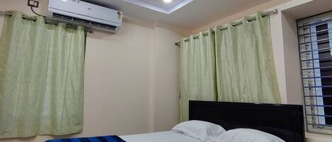 A bedroom with a bed, an air conditioning unit, a ceiling fan, and curtains.