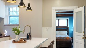 A kitchen with a white countertop, a vase with flowers, and a sink. There is a door leading to a bedroom with a bed and a window. - Beautiful 3BR/2.5 BTH PERFECT location in Short North/Campus w/HUGE 4 car garage (Columbus)