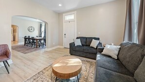 A modern living room with a grey sofa, round coffee table, and a dining area with a wooden table and chairs. - Beautiful 3BR/2.5 BTH PERFECT location in Short North/Campus w/HUGE 4 car garage (Columbus)